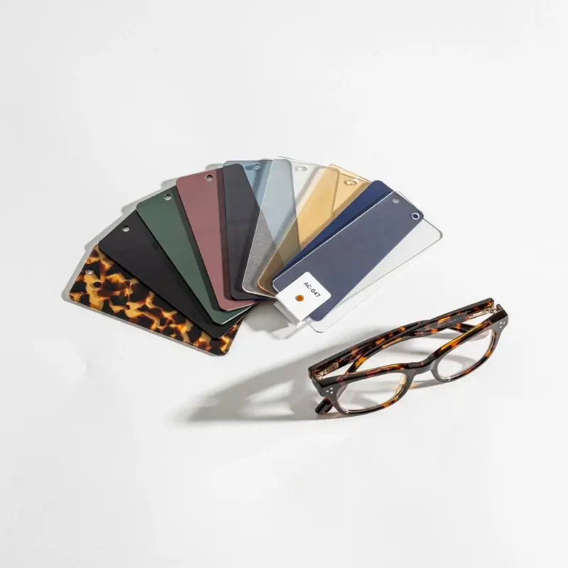 acetate supplier color catalog — fan of acetate color chip samples with reference code card beside finished tortoiseshell sunglasses frame