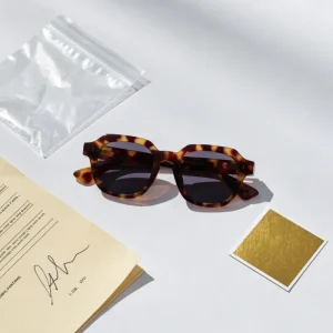 golden sample eyewear manufacturing — tortoiseshell acetate frame beside signed approval document sealed bag and Pantone color reference