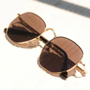 Gold full-rim metal sunglasses with tinted brown lenses and black temple tips resting on a wooden surface in natural light