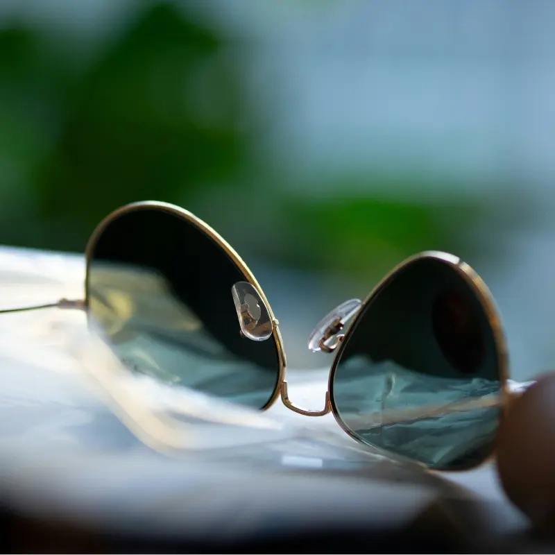 Close-up of gold round metal sunglasses showing the nose bridge and adjustable nose pad arms in natural light