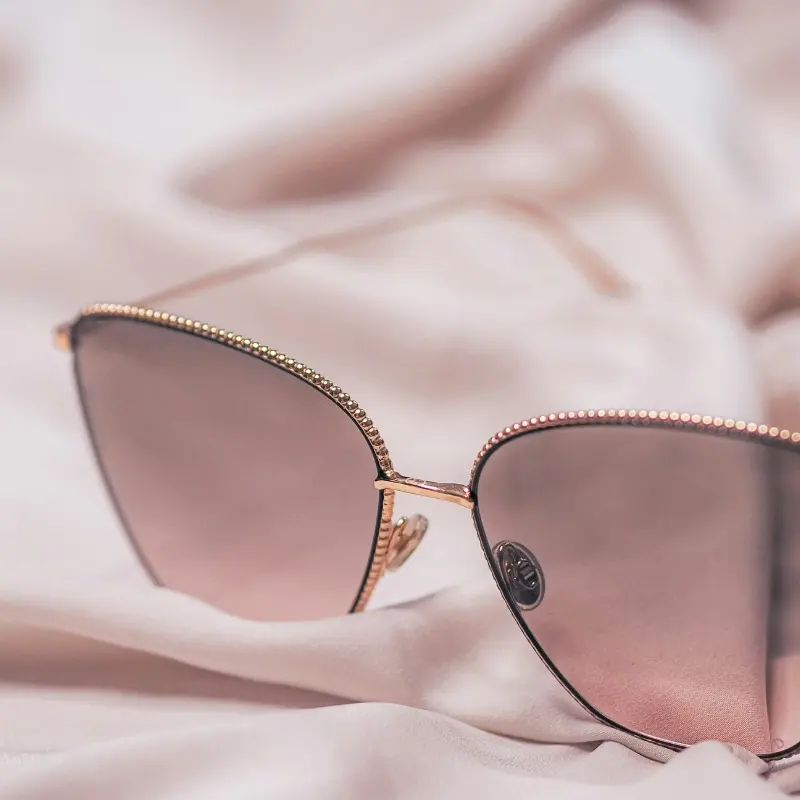 Rose gold metal sunglasses with crystal-embellished frame and gradient pink lenses resting on soft pink fabric