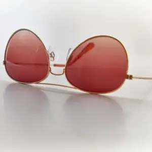 Gold full-rim round metal sunglasses with red tinted lenses and silicone nose pads on white background, close-up sample review angle