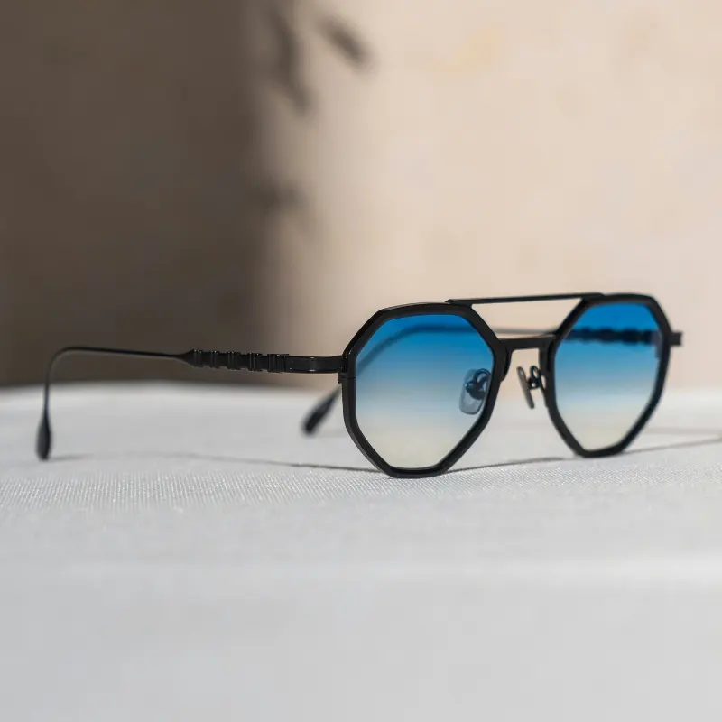 Matte black octagon-shaped metal sunglasses with gradient blue lenses and ribbed temple detail on white fabric background