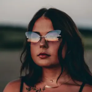 Woman wearing rimless butterfly-shaped metal sunglasses with gradient blue and orange tinted lenses