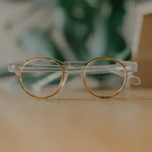 Clear frame round glasses with tortoiseshell lens rims and clear lenses resting on a wooden surface with blurred green plant in background