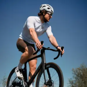 Cyclist wearing custom sports sunglasses with a helmet, riding a road bike against a clear blue sky