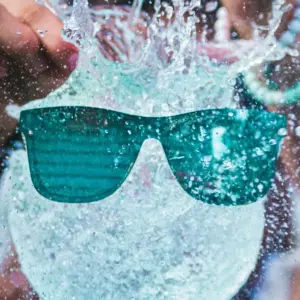 Teal polarized floating sunglasses splashing through water, built for swimming and water sports