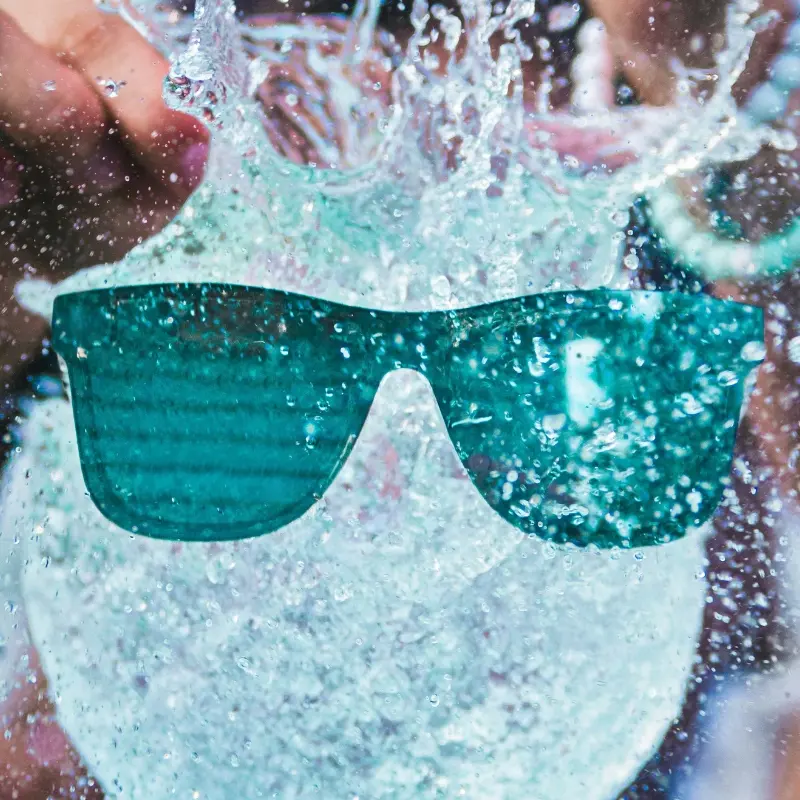 Teal polarized floating sunglasses splashing through water, built for swimming and water sports