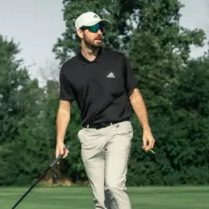 Golfer wearing mirrored sports sunglasses and a cap while walking the course with a golf club