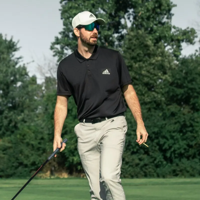 Golfer wearing mirrored sports sunglasses and a cap while walking the course with a golf club