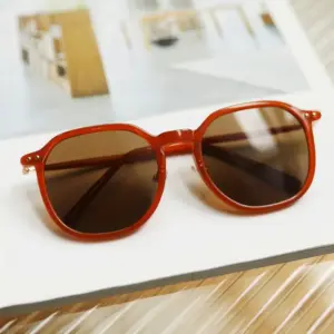Orange full-rim round injection-molded sunglasses with gradient brown lenses and gold rivet hinge detail resting on a white book