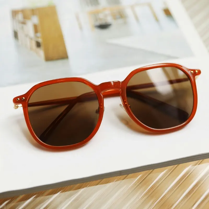 Orange full-rim round injection-molded sunglasses with gradient brown lenses and gold rivet hinge detail resting on a white book