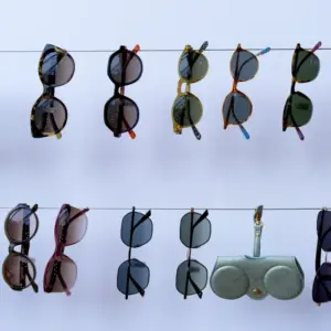 Multiple sunglasses in various frame colors and lens tints hanging on display lines against a white background, showing a range of colorway and lens coating combinations