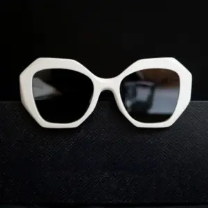 White oversized octagonal injection-molded sunglasses with dark lenses resting on a black textured surface against a dark background