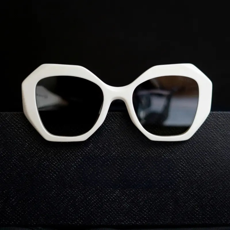 White oversized octagonal injection-molded sunglasses with dark lenses resting on a black textured surface against a dark background