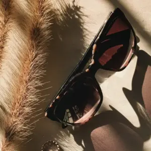 Tortoiseshell cat-eye sunglasses with gradient brown lenses on a beige textured surface with natural light shadows