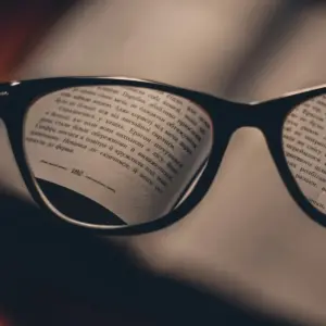 Close-up through black cat-eye reading glasses lenses focused on book text, illustrating the choice between progressive and single-vision reading glasses