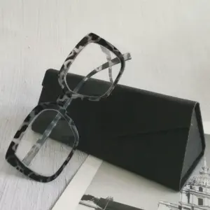 Black and gray tortoiseshell acetate reading glasses leaning on a triangular black hard case, showing private label packaging presentation