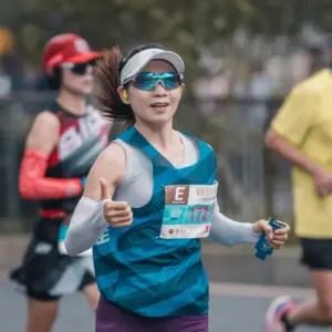 Female marathon runner wearing lightweight running sunglasses and a visor while giving a thumbs up during a race