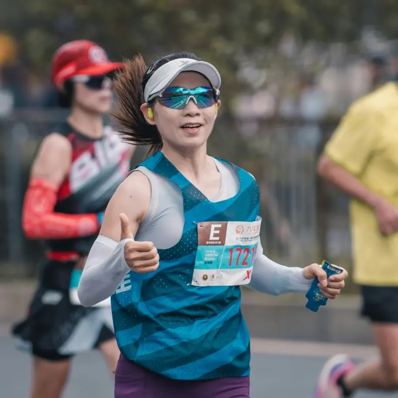 Female marathon runner wearing lightweight running sunglasses and a visor while giving a thumbs up during a race