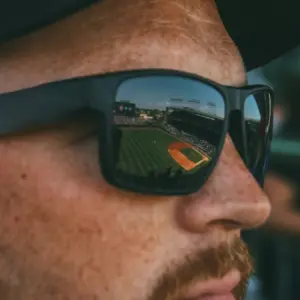 Close-up of a person wearing sports sunglasses with a stadium reflected in the lens