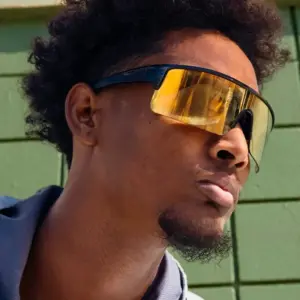 Close-up of a man wearing black shield-style sports sunglasses with a mirrored gold lens