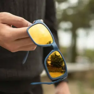 Hand holding blue sports sunglasses with mirrored yellow lenses outdoors for inspection
