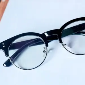 Close-up of black acetate browline eyeglasses with metal lower rim and screw hardware securing the clear lens in place