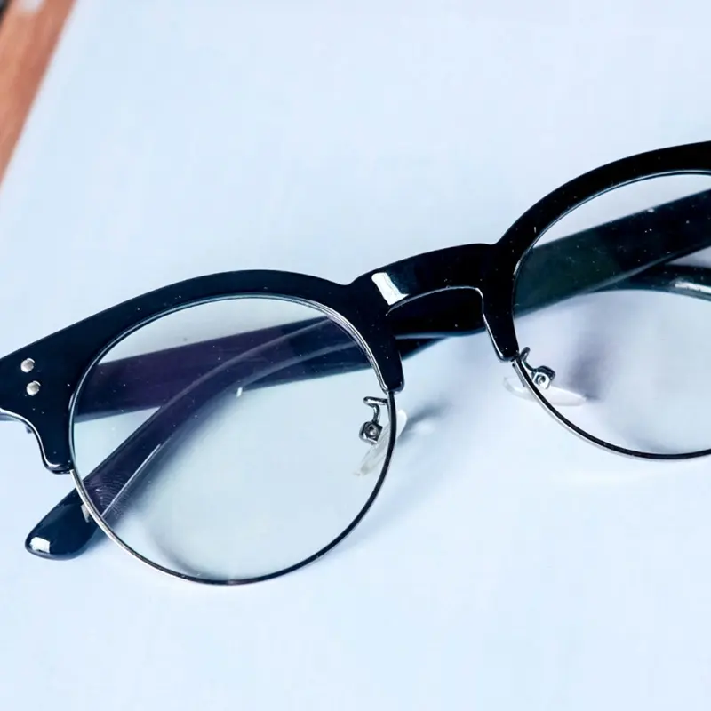 Close-up of black acetate browline eyeglasses with metal lower rim and screw hardware securing the clear lens in place