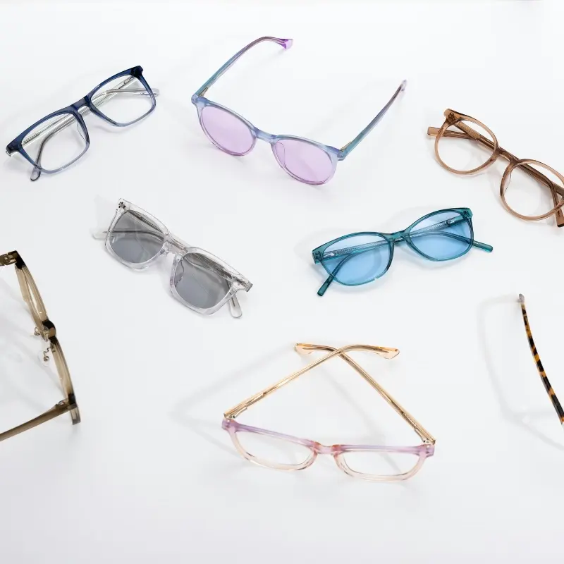 Assorted acetate eyewear frames and sunglasses in multiple translucent colorways scattered on a white background