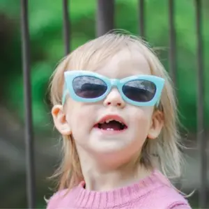 School-age girl wearing bold turquoise cat-eye sunglasses, illustrating a distinctive color and shape choice in kids' eyewear design