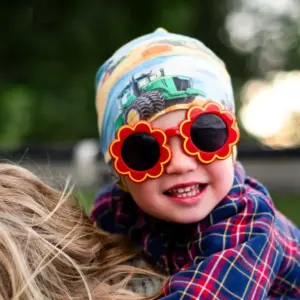 Toddler wearing red flower-shaped sunglasses, illustrating soft frame materials used in kids' sunglasses