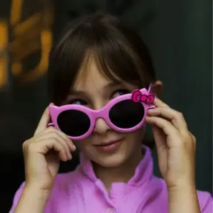 Child holding up pink round sunglasses with a decorative bow accent on the frame