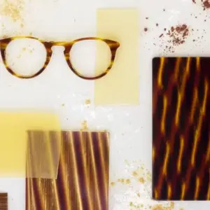 Tortoiseshell acetate eyeglass frame beside raw acetate sheet samples, showing the color depth and pattern layering associated with premium Mazzucchelli-grade acetate