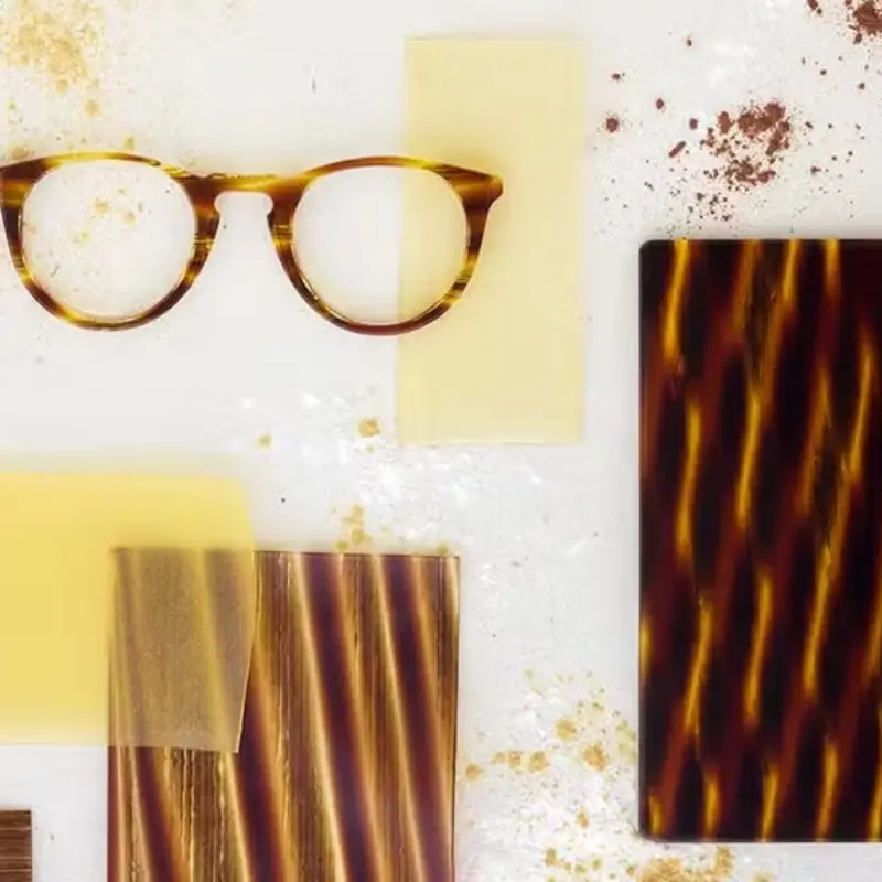 Tortoiseshell acetate eyeglass frame beside raw acetate sheet samples, showing the color depth and pattern layering associated with premium Mazzucchelli-grade acetate