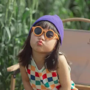 Young girl wearing round orange sunglasses outdoors, illustrating everyday UV protection for children's eyewear